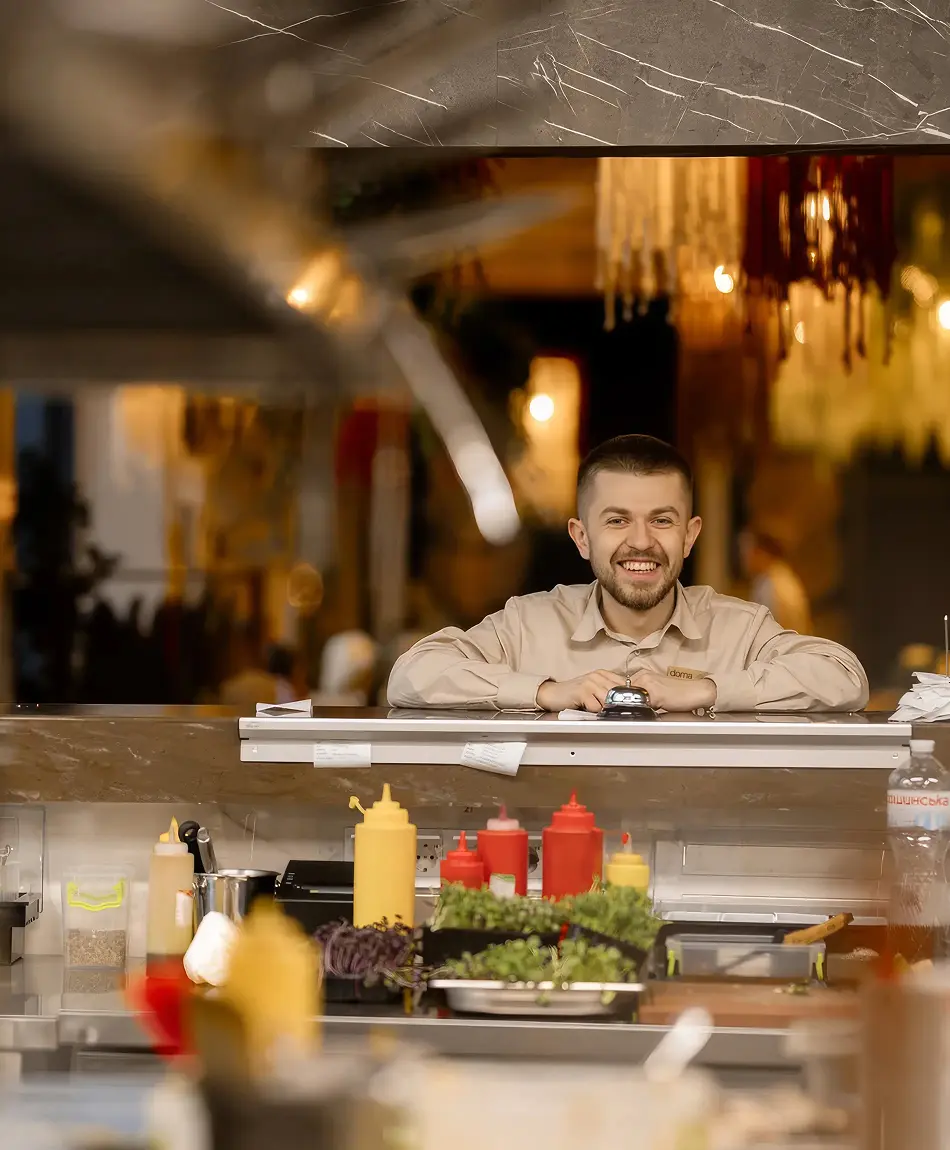 Офіціант ресторану doma посміхається у камеру на фоні закладу.