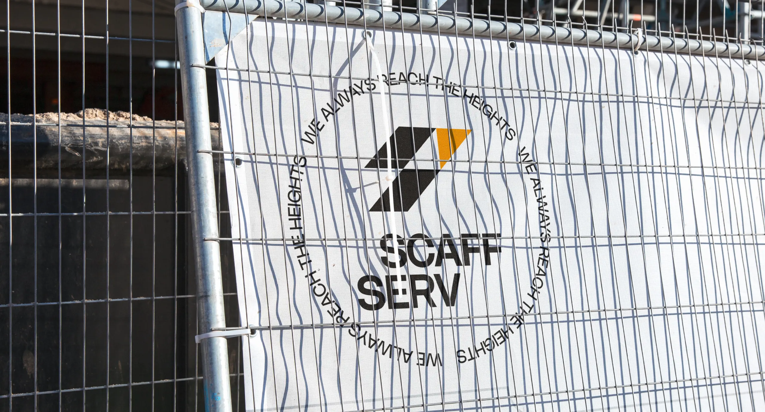 Банер з фірмовим штампом Scaff Serv за огородженням на будівництві.