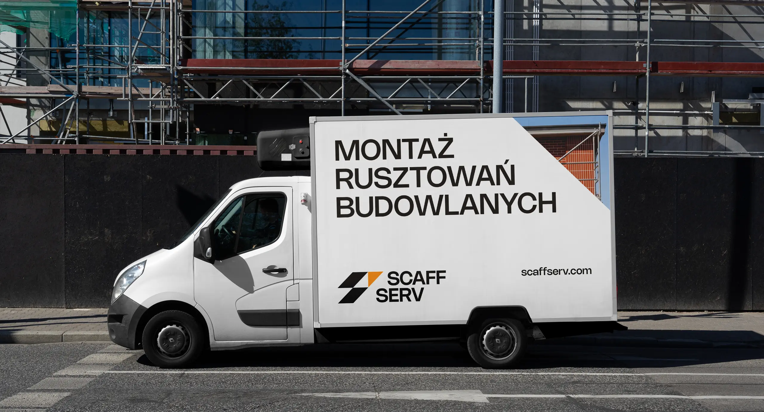 Брендована вантажівка Scaff Serv на фоні будинку під час будівництва з риштуванням уздовж фасаду.